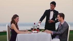 People eating in hotel restaurant, wife, husband, couple, man at work as waiter serving wine to clients celebrating honeymoon on resort veranda. Relax, fun, leisure, romance, romantic dinner. 3of7 - Powered by Shutterstock - Get 15% off with code: PIKWIZARD15