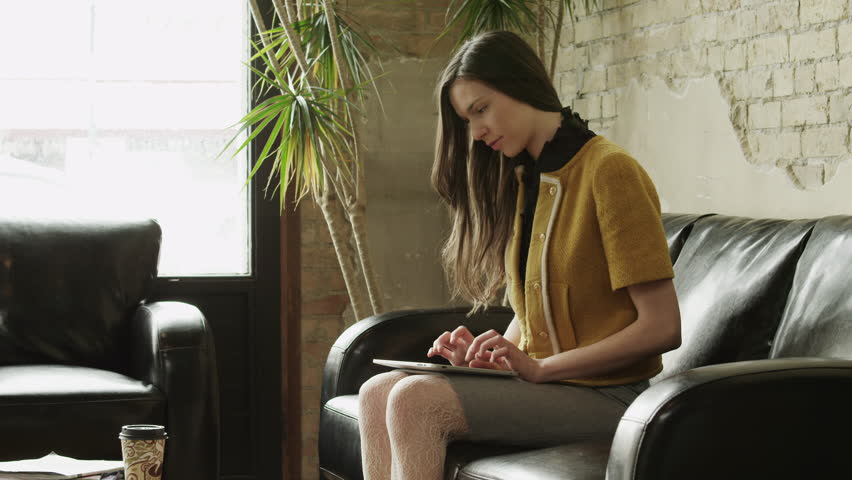 Medium Shot Young woman typing on digital tablet sitting on sofa in waiting room 