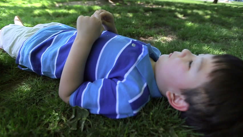 Six Year Old Laying Down In The Grass, Under A Tree, Looks Up Peacefully