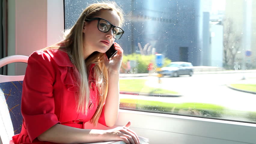 Young blond woman riding tram, talking on mobile phone