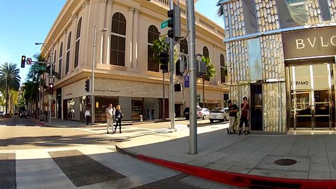 BEVERLY HILLS, CA: March 10, 2014- People walking on Rodeo Drive circa 2014 in Beverly Hills. A bright red Farrari passes through an intersection near exclusive and expensive retail stores.
