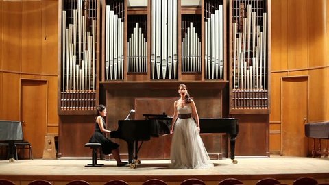 Woman pianist plays the piano and singer emotionally sing opera song at stage