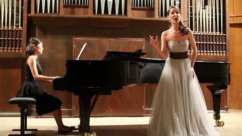 Woman pianist plays the piano and beautiful singer emotionally sing opera song at stage