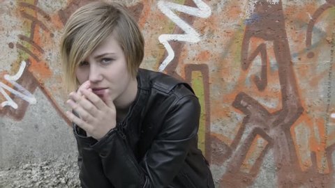 Anxious, depressed teenage girl sitting outside school, with graffiti covered wall as background