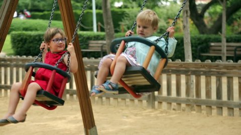 Laughing children on swing in summer park