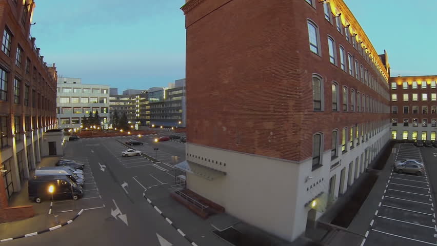Parking place with cars near edifice with illumination at evening. Aerial view