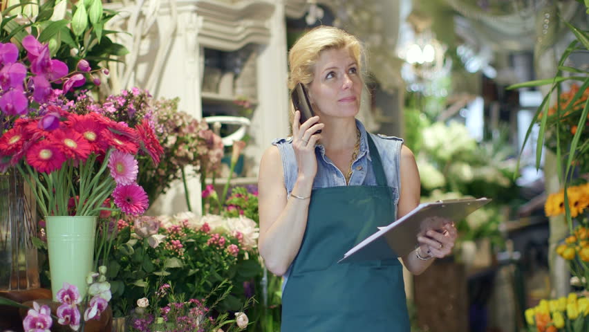 A Florist speaks on the phone, inspecting the supplies in her shop and noting it on her clipboard Royalty-Free Stock Footage #6441074