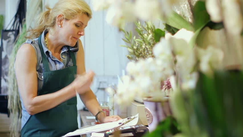 A Florist stands in her shop speaking on the phone, writing notes and inspecting the shop's supplies Royalty-Free Stock Footage #6441089