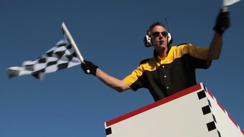 Slow motion version of race official waving a checkered flag at an auto race. View is from the track looking up.