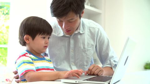 Asian Father Helping Son To Use Laptop At Home