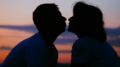 silhouettes of young man and woman kissing, sunset sky in background 