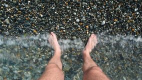 male foots of adult man standing in sea surf, first person video 