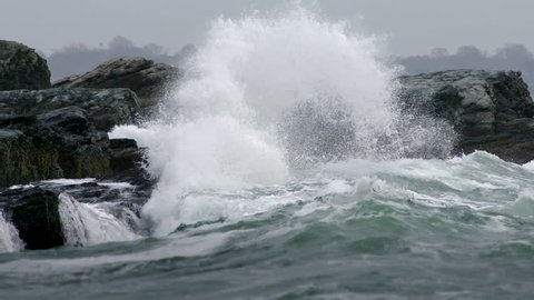 Big heavy waves crash into a rocky cliff and spray mist everywhere, in slow motion