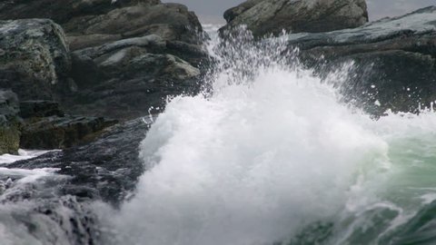 Waves crash against the rocky coast, in slow motion