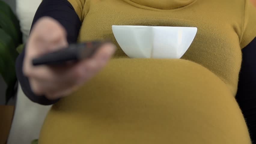 Pregnant woman watches television while eating snack
