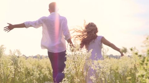 Happy couple having fun outdoors. Couple running away being excited with the freedom of the countryside. Young Man and woman holding hands and running through a field with wild flowers. Slow motion