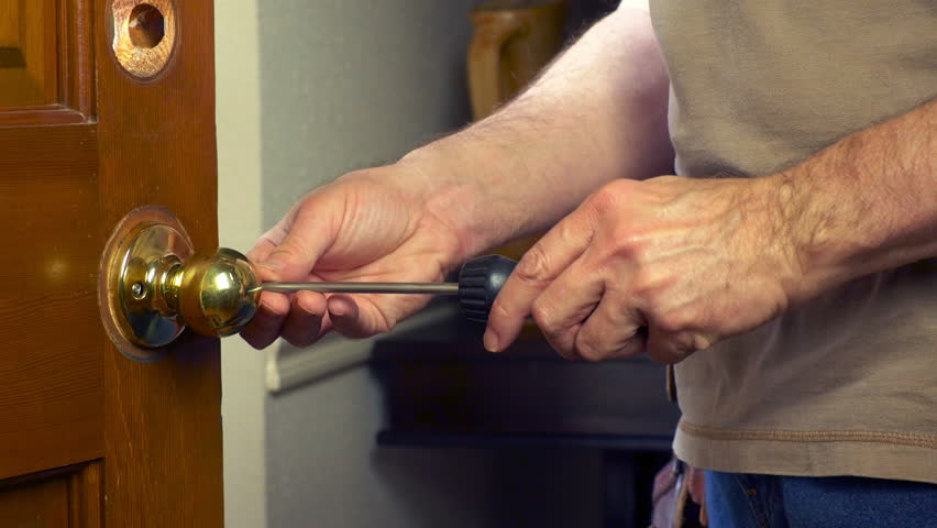 A handyman removing a door knob from a front door.