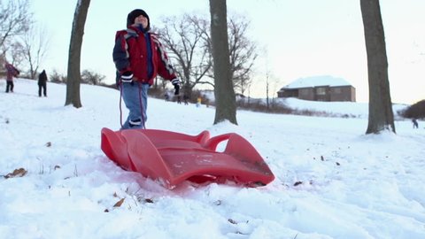 Young boy running up hill with sled