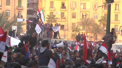 Large crowd of demonstrators inside Tahrir Square, Cairo on 1st anniversary of Egyptian Revolution.  Men wave Egyptian flags, revolutionary Syrian flags, Arabic banners.   25 Jan 2012