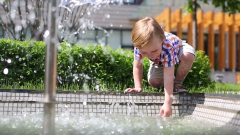 Little boy touches water from fountain in summer park