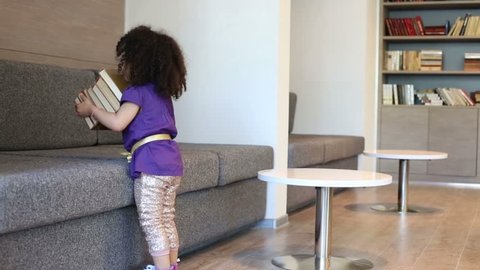 Little cute girl carries stack of books in business center