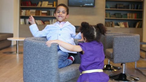 Happy sister whirls her brother on armchairs in business center
