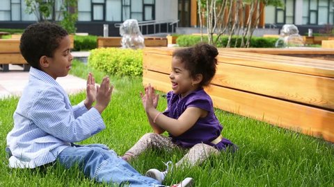 Brother and sister sit on grass and clap each other hands