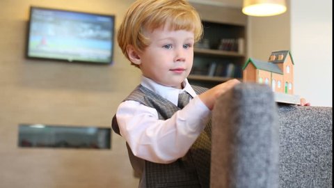 Little cute boy plays with toy on armchair house in business center