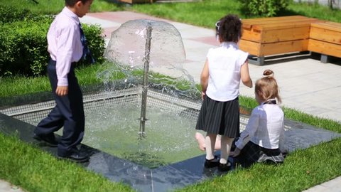 Four children in business clothes play near fountain in summer park