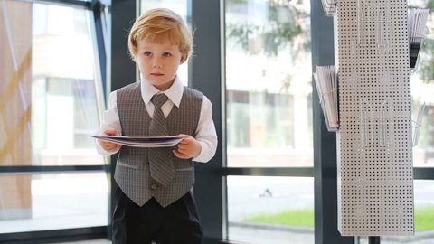 Little boy in business clothes with magazine in business center