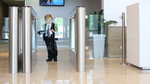Little happy boy in suit with tie goes glass turnstile in business center
