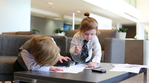 Boy plays with stapler and girl draws with ruler in business center