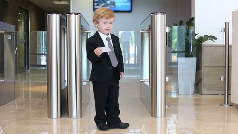 Little boy in suit stands near entrance to business center with card