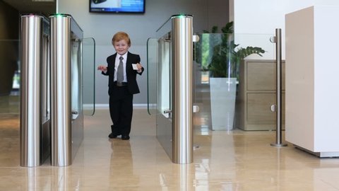 Little cute boy in suit goes glass turnstile in business center