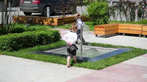 Little boy and girl in business clothes play near fountain in summer park