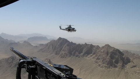 Marine Huey Helicopter (UH-1) flying over the mountainous terrain is silhouetted by door gunner and machine gun