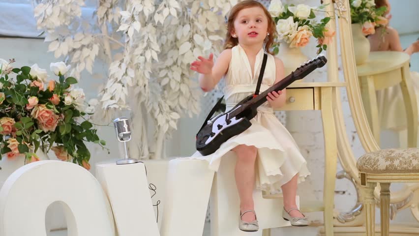 Beautiful little girl in white dress sings and plays guitar