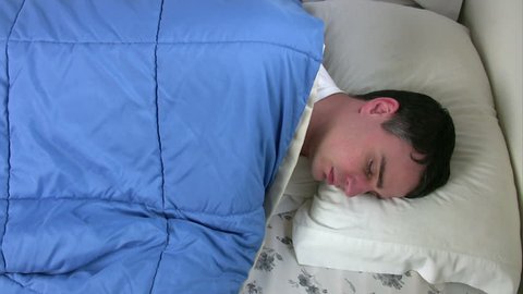 Man sleeping comfortably in bed, rolls onto his back with hands behind head.