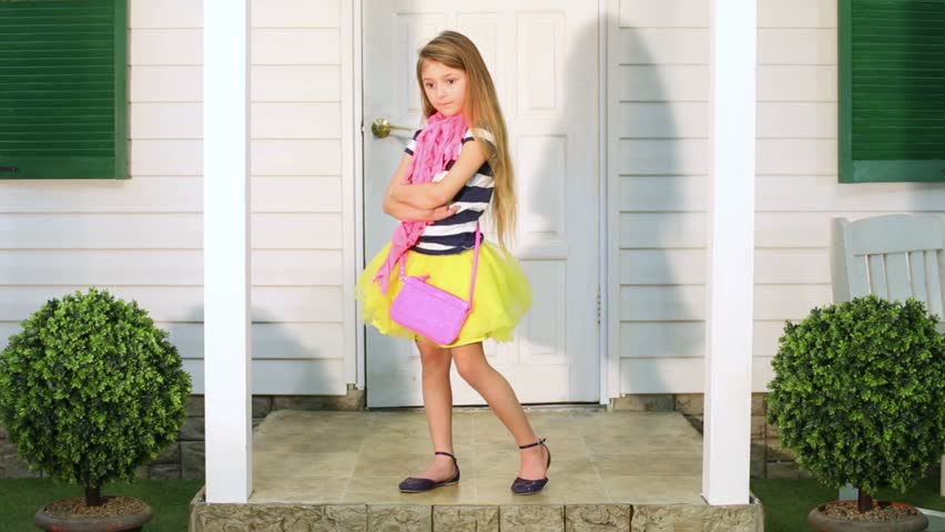 Little girl enters house door, then comes out and stands on porch with her hands akimbo.