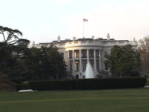 White House / lawn with flag waving on top and fountain flowing in front of it. Close up shot.