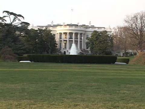 White House / lawn with flag waving on top and fountain flowing in front of it. Close up shot which zooms back slowly.