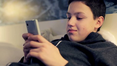 Young boy with smartphone lying on bed at night
