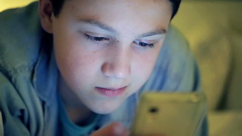 Closeup of young boy looking at smartphone at night
