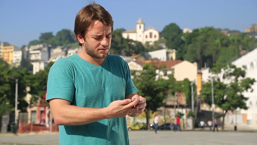 A young man on the street uses his cell phone to take a selfie