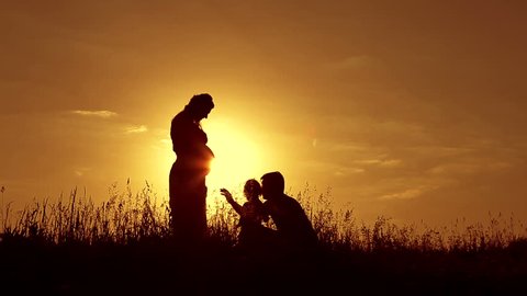 Beautiful shot of happy family: pregnant mother, father and little daughter at sunset. Silhouettes.