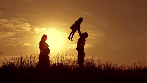 Beautiful shot of happy family: pregnant mother, father and little daughter at sunset. Silhouettes.