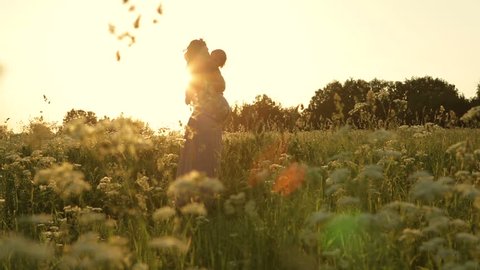 Young pregnant woman holding a baby daughter. Beautiful sunset in the meadow. Dolly shot.