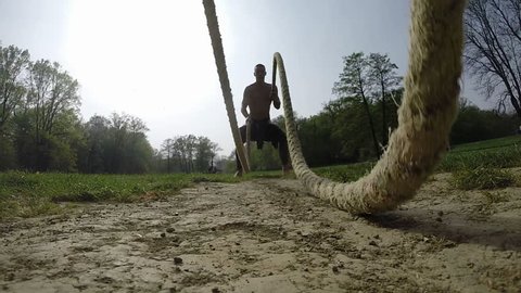 Muscular man doing waves with undulation ropes