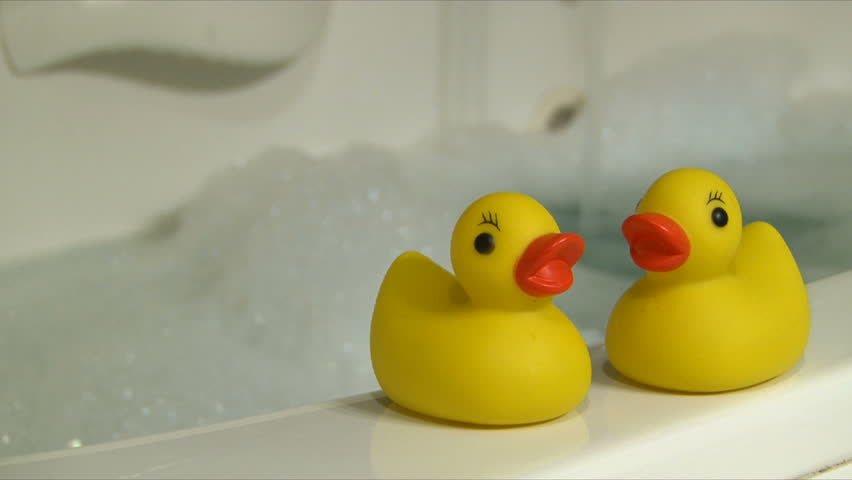 Rubber duckies and bubble bath with woman stirring in hot water.
