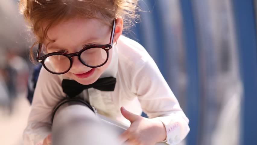 Little cute girl in glasses climbs on railing near windows